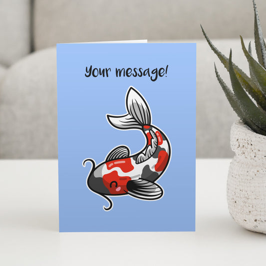 A blue greeting card standing on a white table with a design of a red white and grey koi carp fish facing to the left and the words your message written above