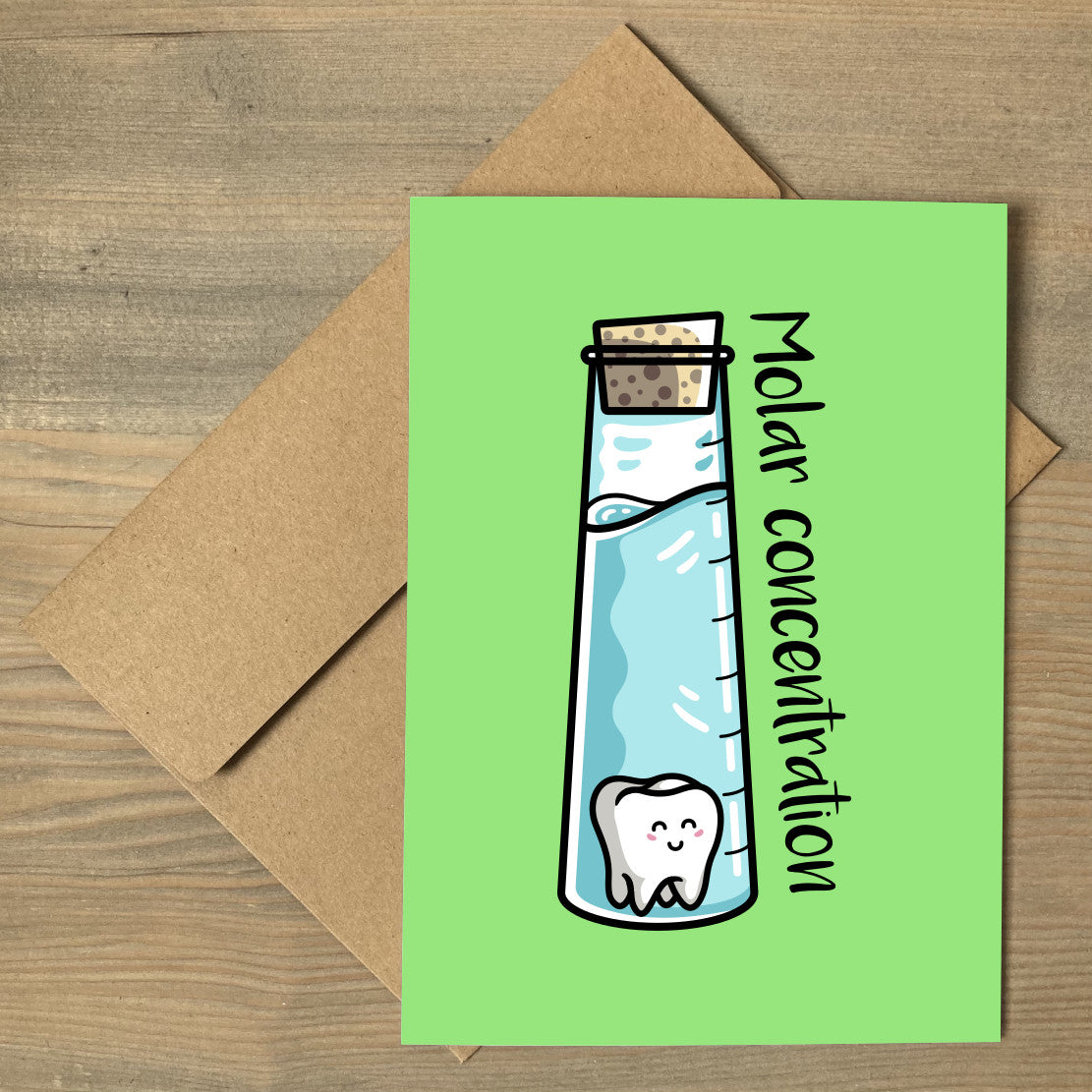 A brown envelope beneath a green greeting card with a design of a corked tall chemistry vessel of liquid containing a kawaii cute molar tooth with the words molar concentration written at an angle along the right hand length of the glass vessel