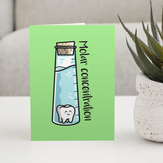 A green greeting card standing on a white table with a design of a corked tall chemistry vessel of liquid containing a kawaii cute molar tooth with the words molar concentration written at an angle along the right hand length of the glass vessel