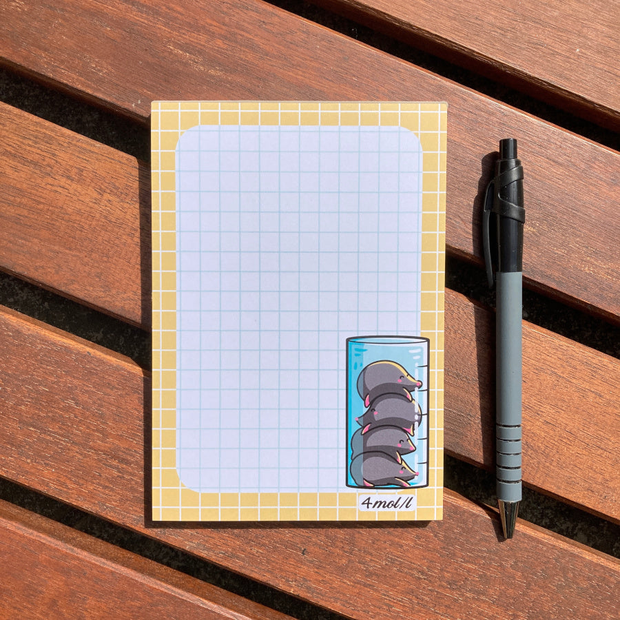 A white notepad with a sandy yellow border and blue graph lines. In the bottom right hand corner is a design of four cute moles inside a chemistry cylinder.