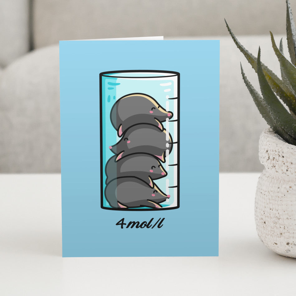 A blue greeting card standing on a white table with a design of a chemistry beaker filled with 4 kawaii cute moles in a pile on top of each other and 4mol/l written beneath