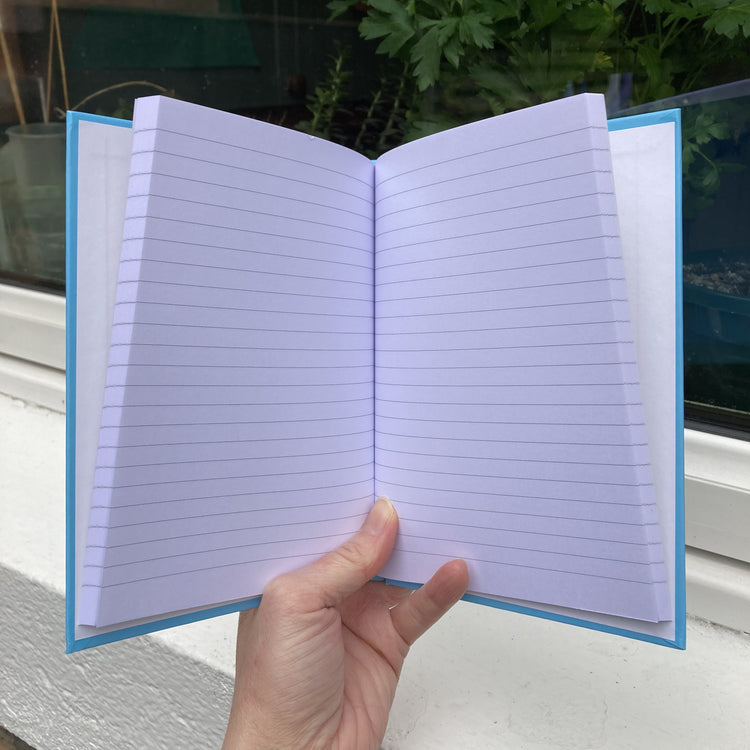 Hardback journal held open in a hand showing lined pages within