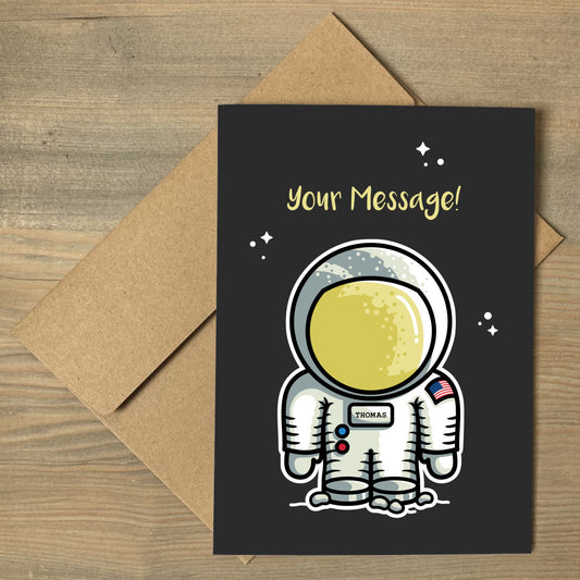 A brown envelope beneath a black greeting card that features a cute astronaut space suit with a personalised name on its chest and a personalised message above.