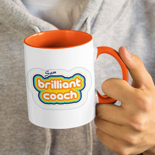 Personalised stripey brilliant coach design on a two toned orange and white ceramic mug, being held in a hand.