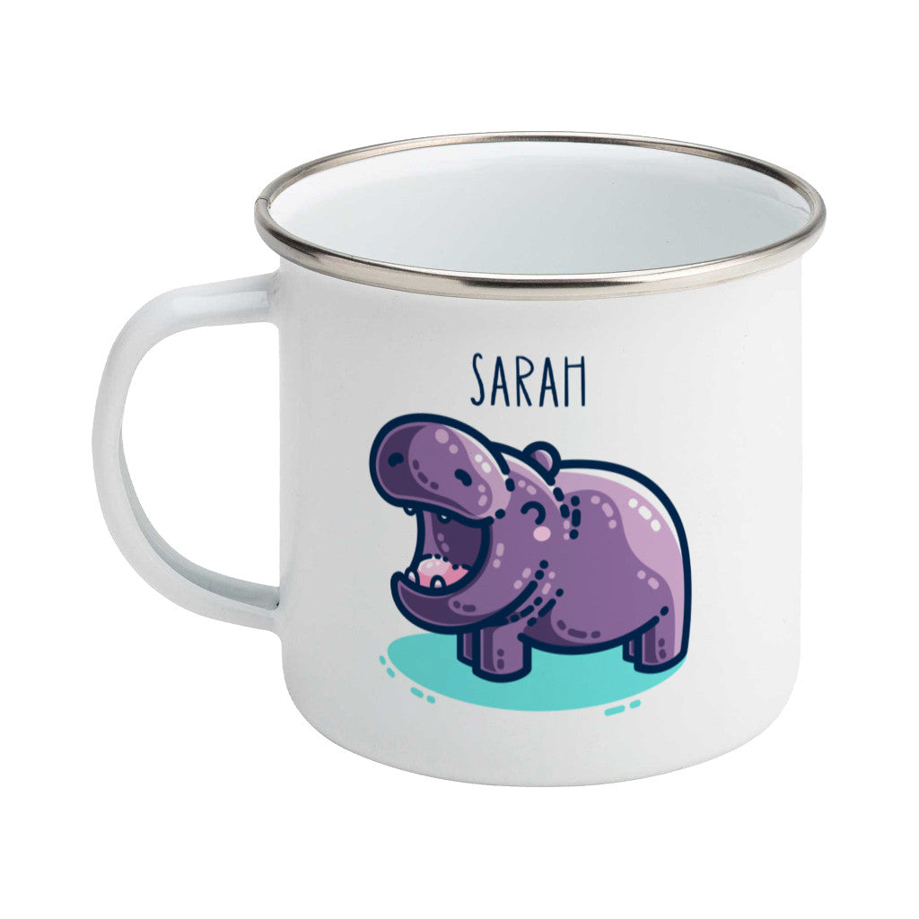 A white enamel mug with a silver rim, handle to the left. A name is written in thin dark blue upper case letters above a kawaii cute purple hippo with a thick dark blue outline and a turquoise shadow beneath. The hippo is seen side on facing to the left and looks happy with its mouth open wide.