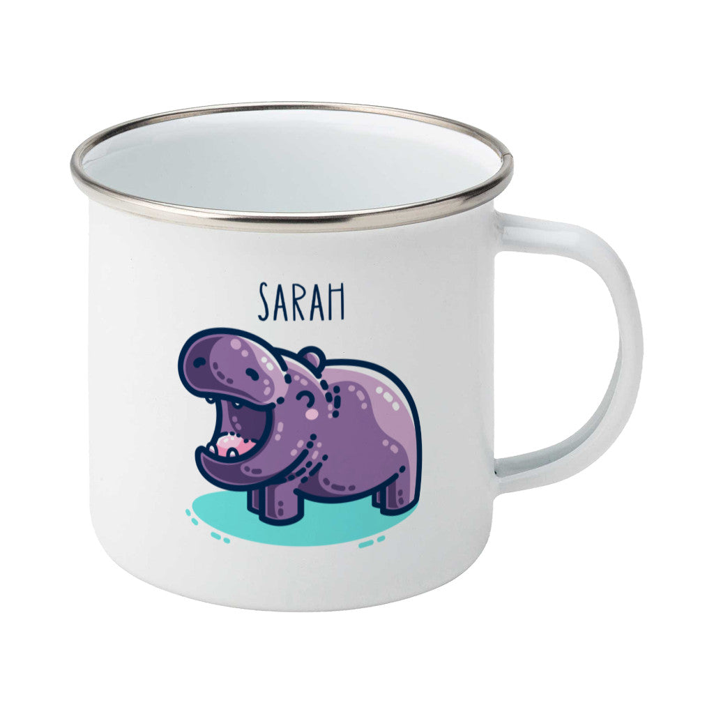 A white enamel mug with a silver rim, handle to the right. A name is written in thin dark blue upper case letters above a kawaii cute purple hippo with a thick dark blue outline and a turquoise shadow beneath. The hippo is seen side on facing to the left and looks happy with its mouth open wide.
