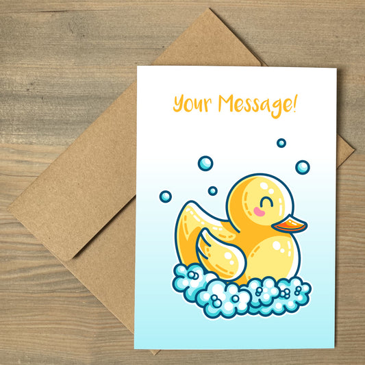 A white to blue gradiant greeting card lying flat on a brown envelope, with a design of a kawaii cute yellow rubber duck surrounded by bubbles and personalised with your message above