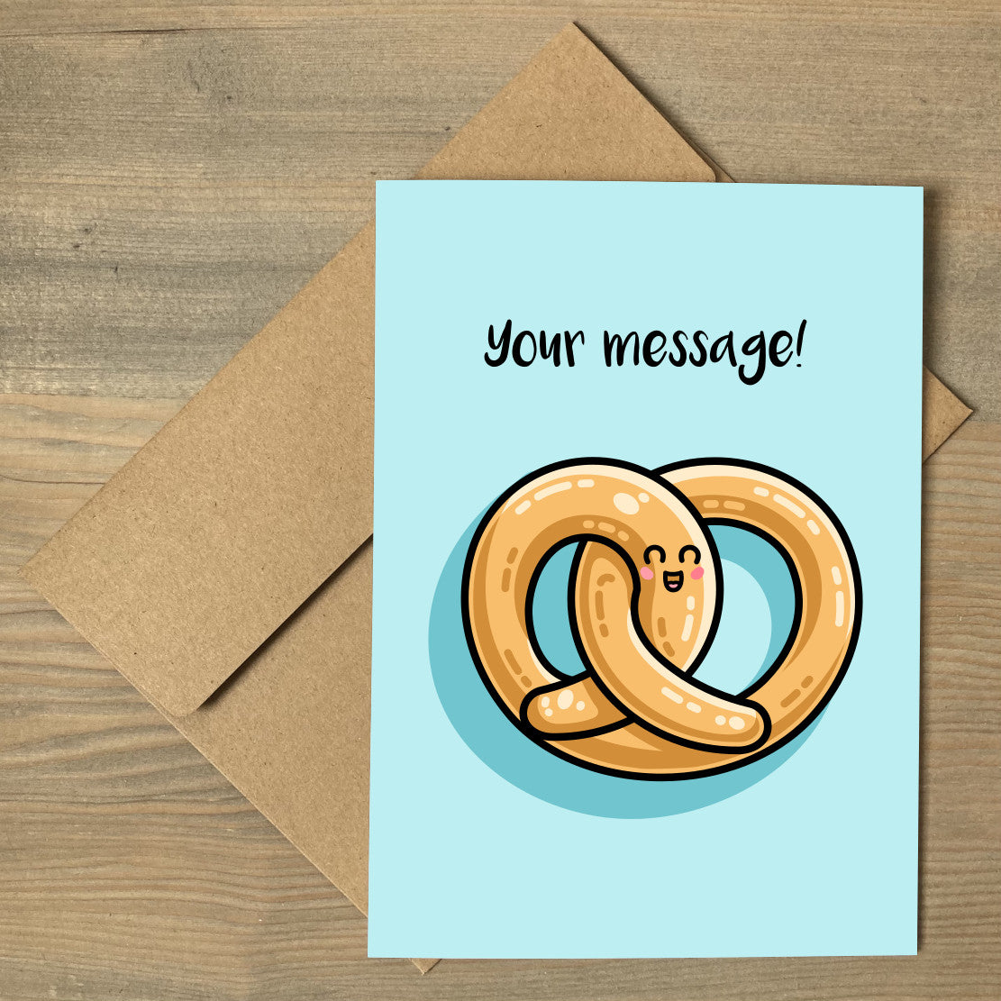 A pale turquoise greeting card lying flat on a brown envelope, with a design of a kawaii cute pretzel and personalised with your words above