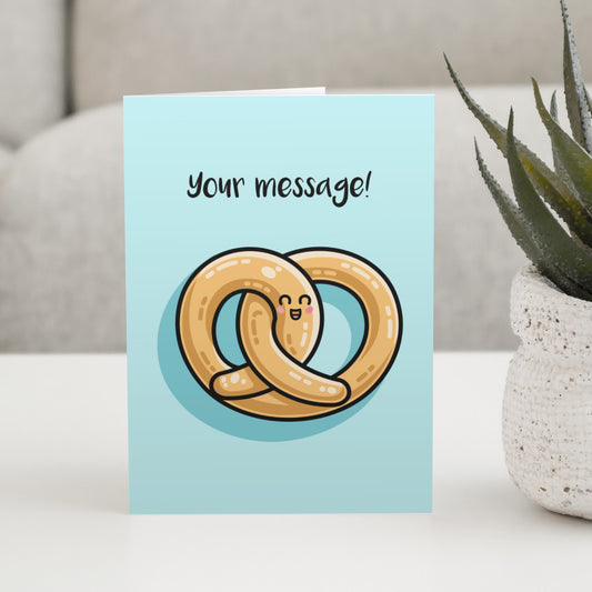 A pale turquoise greeting card standing on a table with a design of a kawaii cute pretzel and personalised with your words above