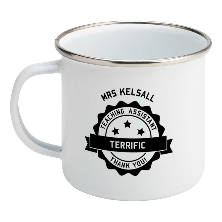 Personalised black circular banner design with the words 'terrific teaching assistant' on a silver rimmed white enamel mug, showing LHS
