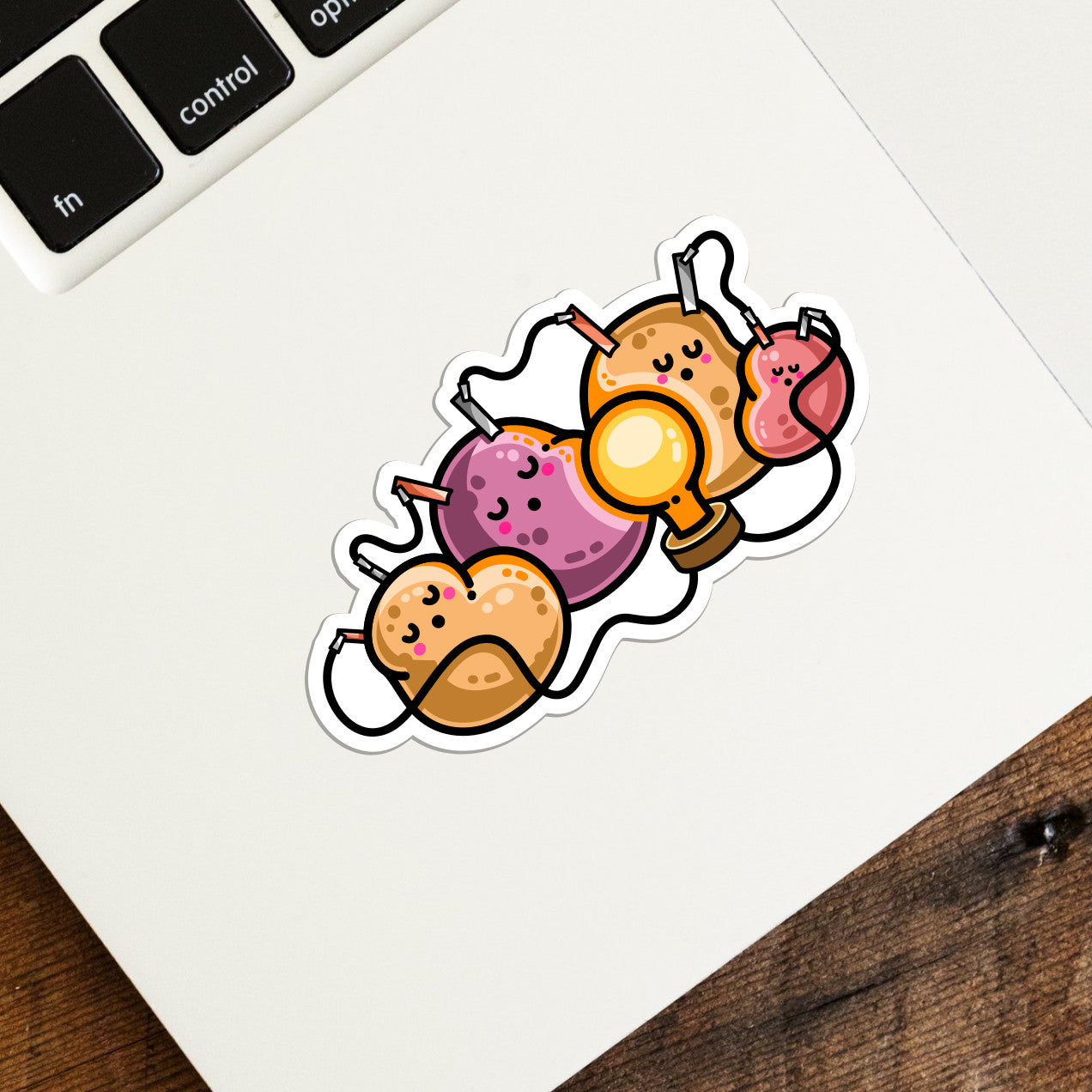 A white die cut vinyl sticker on the corner of a laptop keyboard. Design is of a potato battery of 4 potatoes asleep around a light bulb they are powering.