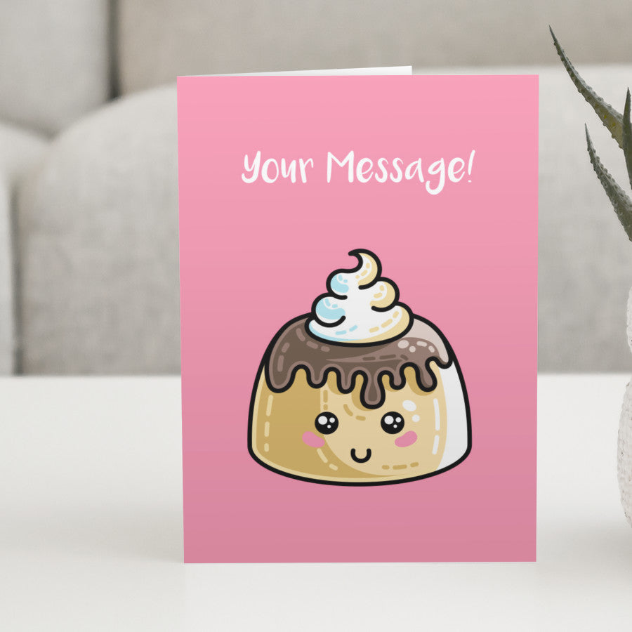 A pink greeting card standing on a white table, with a design of a kawaii cute sponge pudding with cream and chocolate sauce on top and a personalised message above