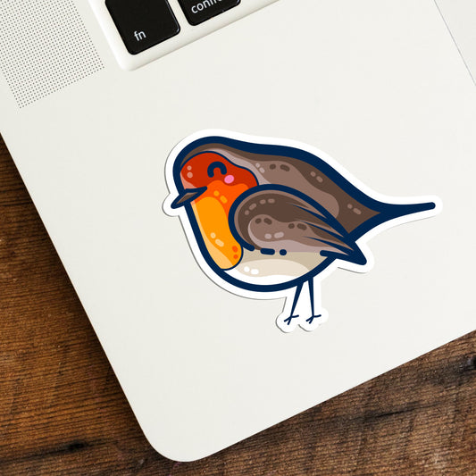 The bottom left hand corner of a laptop keyboard with a vinyl kiss cut sticker on it of a robin bird in a kawaii cute style facing to the left with the usual white border around the shape of the sticker