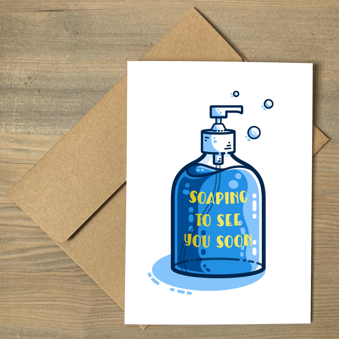 A white card lying flat on a brown envelope. The card has a picture of a bottle of blue liquid soap on it and the yellow words on the bottle say soaping to see you soon.