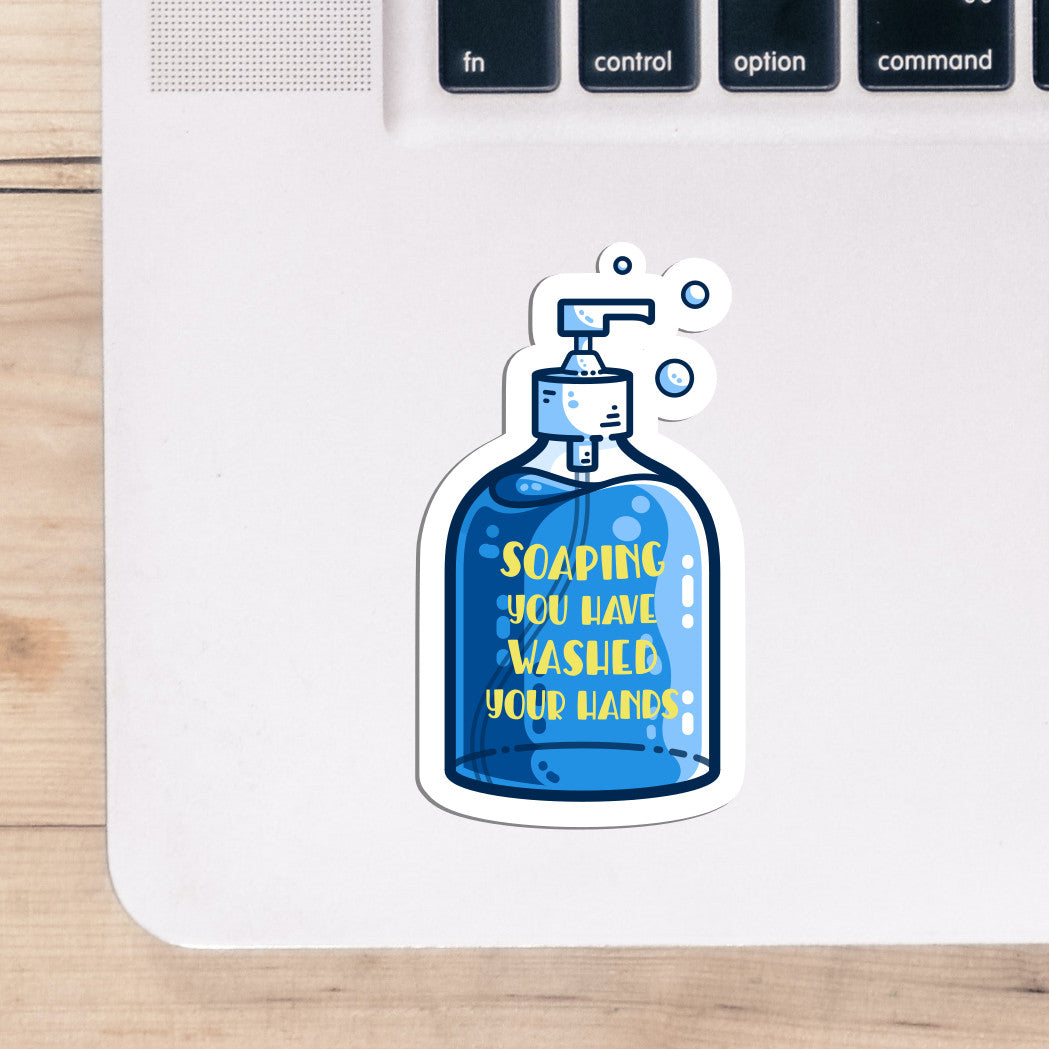 The corner of a laptop keyboard with a sticker on it. The sticker is of a soap dispenser bottle full of blue liquid soap and has the words 'soaping you have washed your hands' on the bottle in yellow capital letters.