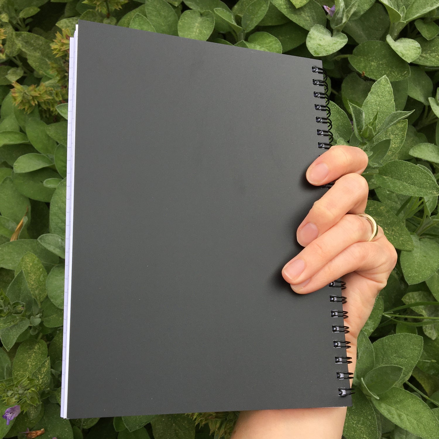A hand holding a closed notebook showing the black back cover