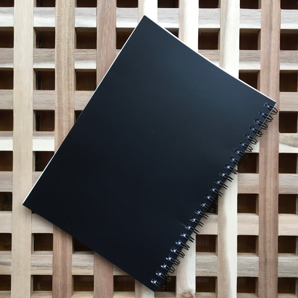 Black spiral notebook lying flat on a wooden surface showing the plain black back cover of the notebook