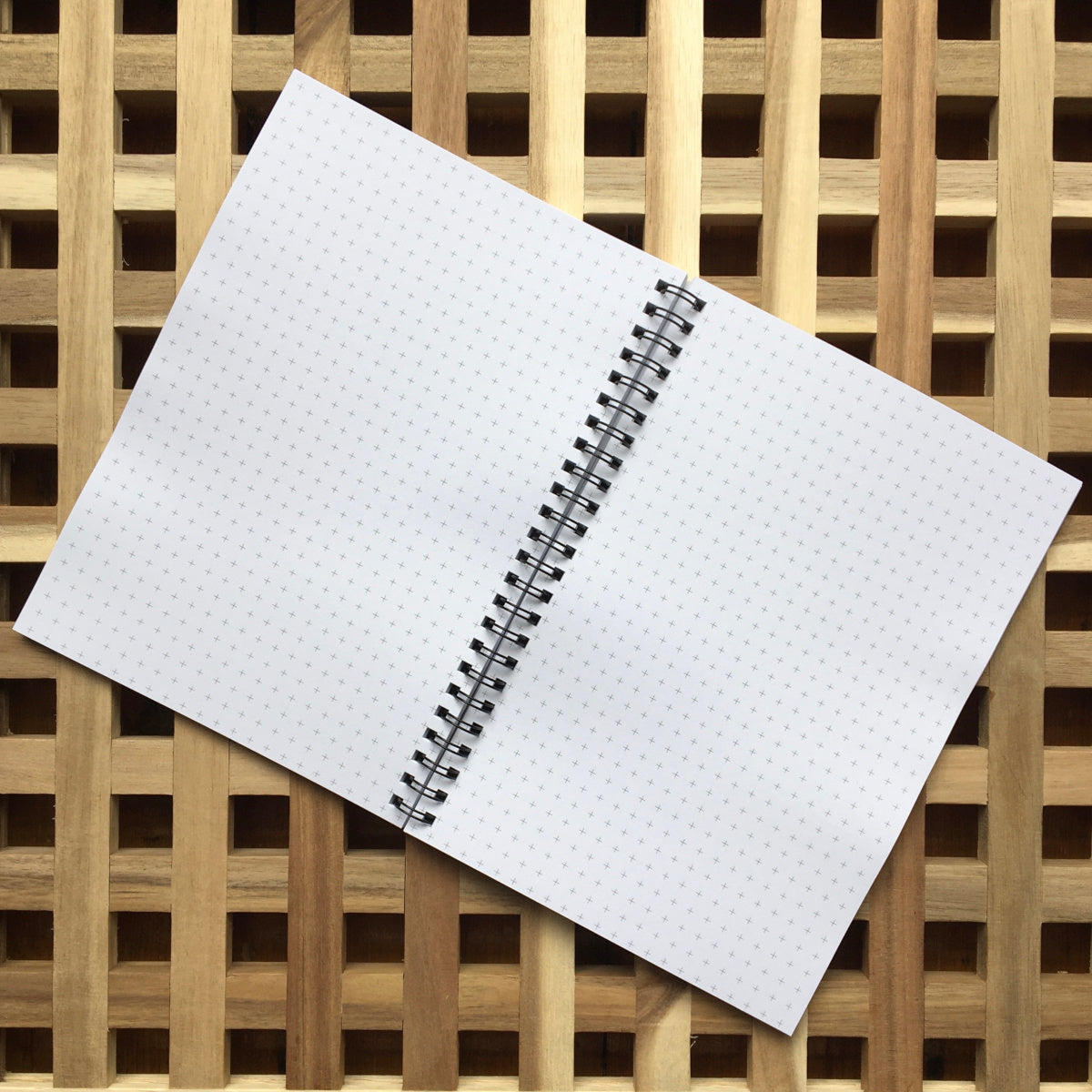 Spiral bound notebook lying open and flat showing pages of grid graph paper like little crosses all over the white paper
