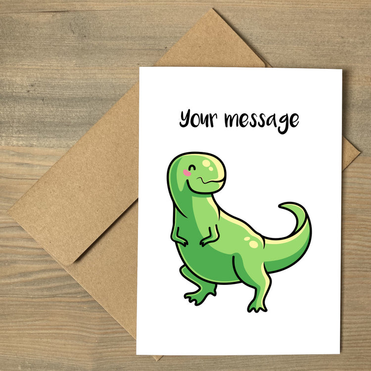 A white greeting card lying flat on a brown envelope, with a design of a cute green tyrannosaurus rex with a personalised message above
