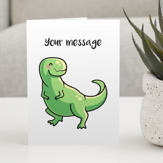 A white greeting card standing on a white table, with a design of a cute green tyrannosaurus rex with a personalised message above