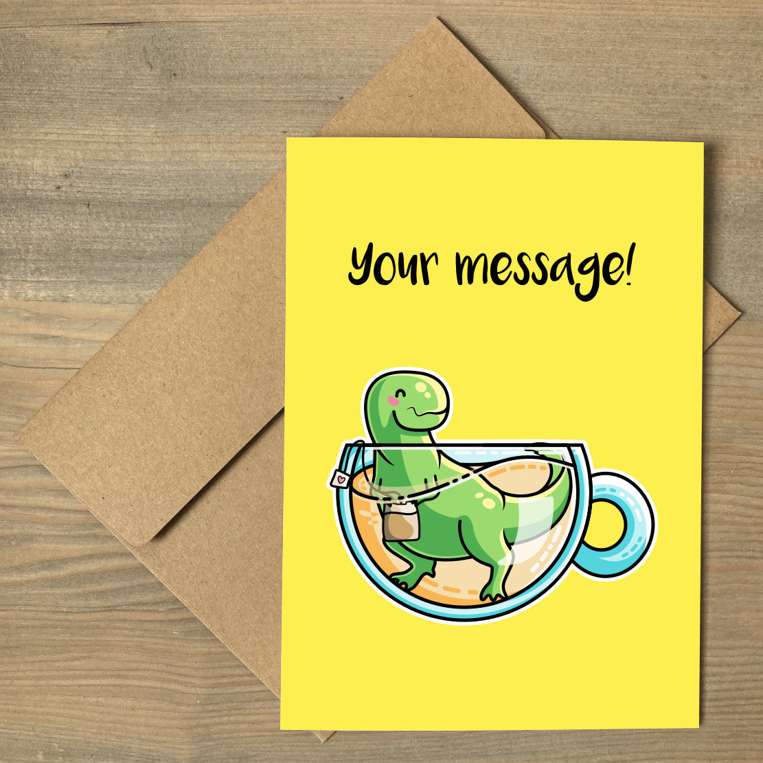 A yellow greeting card lying flat on a brown envelope, with a design of a cute green tyrannosaurus rex dinosaur holding a teabag in a glass teacup of yellow liquid with a personalised message above
