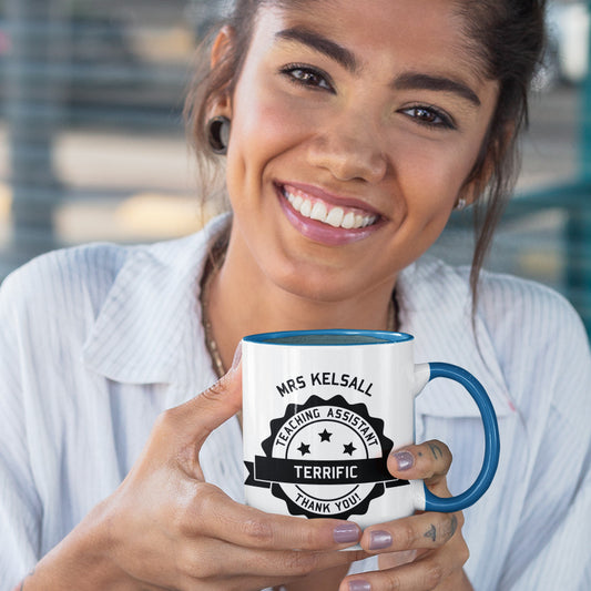 woman holding a personalised black circular banner design with the words 'terrific teaching assistant' on a two toned blue and white ceramic mug