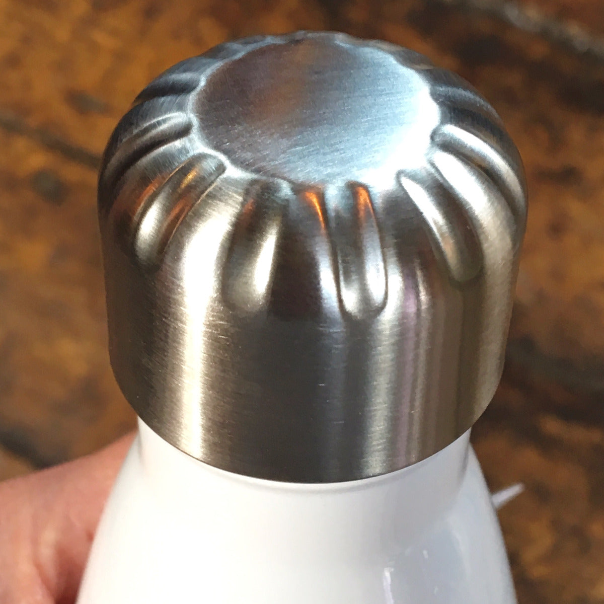 Photo showing brushed and indented pattern silver lid on white bottle.