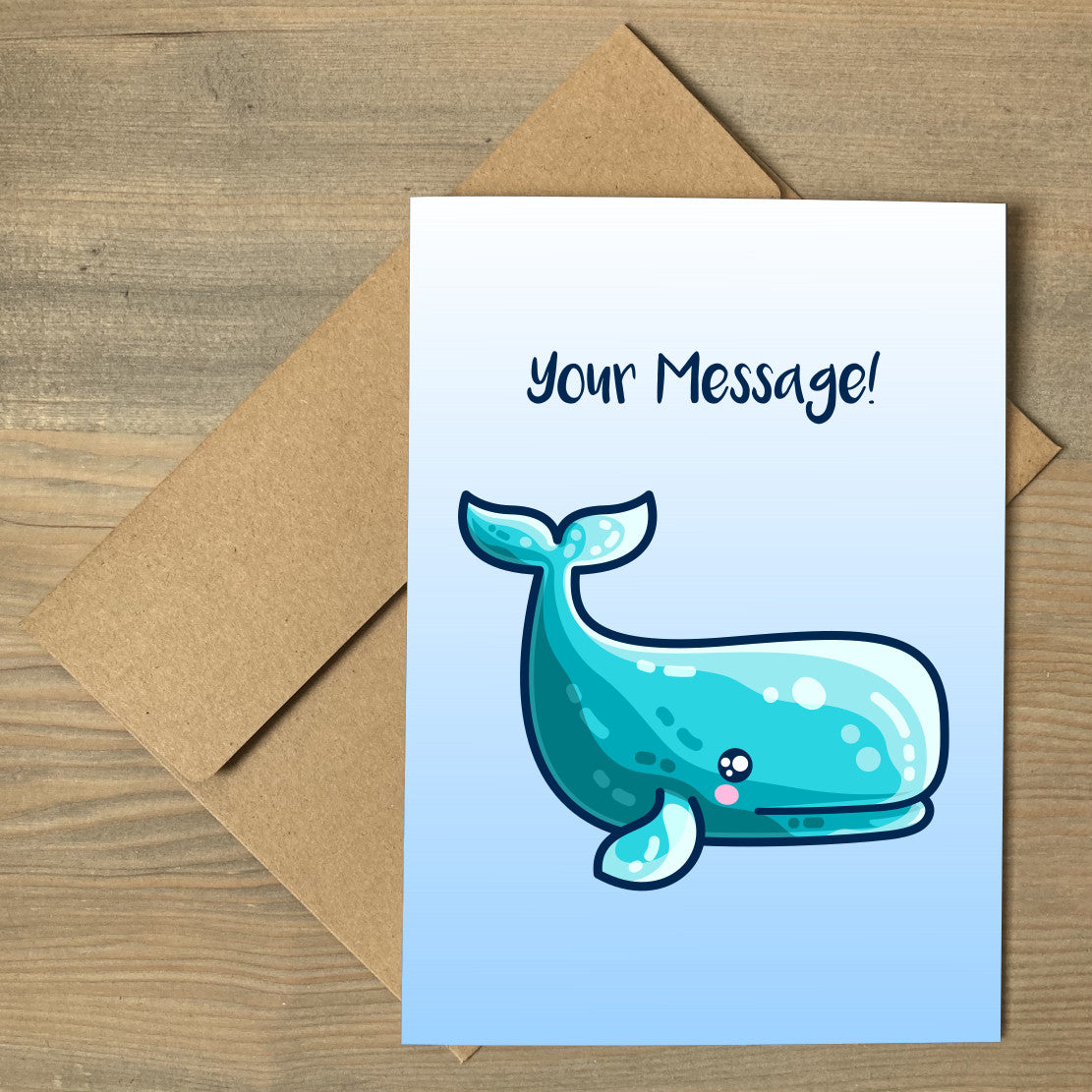 A white to blue gradiant greeting card lying flat on a brown envelope, with a design of a kawaii cute sperm whale looking to the right and a personalised message above
