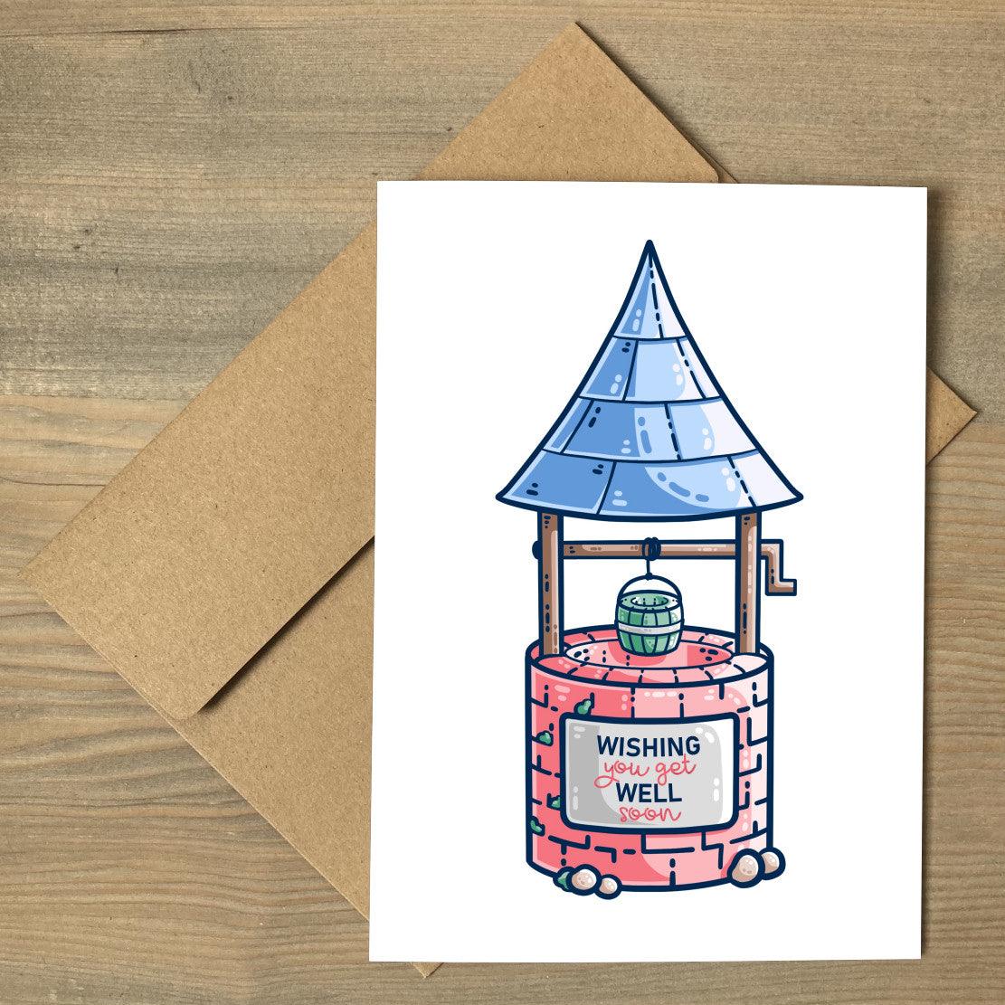 A white greeting card lying flat on a brown envelope, with a design of a wishing well with blue pointy roof, green bucket, red stone and a sign with the words wishing you get well soon